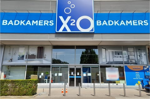 x²o badkamers showroom in Zaventem met blauwe gevel, glazen ramen en zicht op badkameropstellingen binnenin.