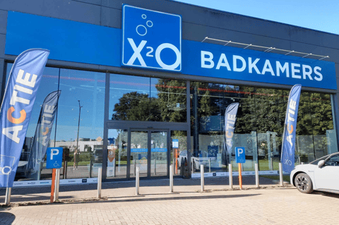 Magasin X²O salles de bains avec façade vitrée, portes automatiques et drapeaux promotionnels à l’entrée – X²O salles de bains