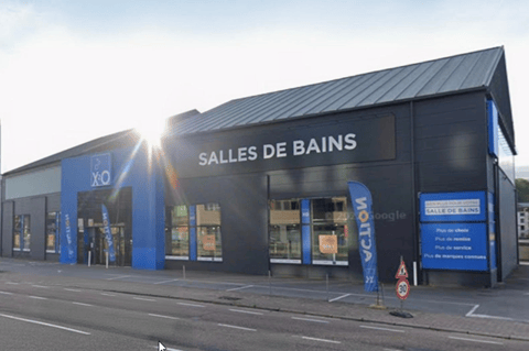 Magasin X²O salles de bains avec façade sombre, grandes vitrines et lumière du soleil à l’avant – X²O salles de bains