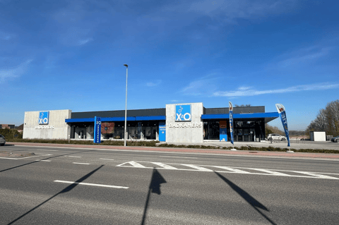 Showroom moderne X²O salles de bains le long d’une large route, avec façade vitrée, accents bleus et drapeaux à l’entrée – X²O salles de bains