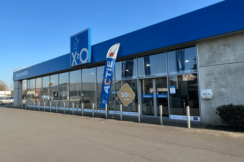 Spacieux showroom X²O salles de bains avec longue façade vitrée, branding reconnaissable et signalisation promotionnelle jusqu’à -50%, invitant à découvrir de nombreux aménagements de salles de bains à l’intérieur – X²O salles de bains