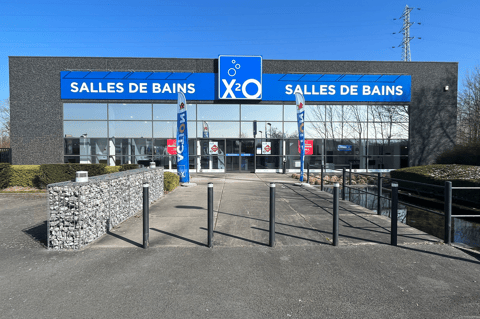 Showroom moderne X²O “Salles de bains” avec entrée centrale, façade symétrique et branding clair, entouré d’un espace extérieur soigné et d’un chemin d’accès – X²O salles de bains