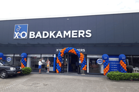 Feestelijk aangeklede X²O Badkamers showroom met opvallende ballonnenbogen aan de ingang en duidelijke branding, die klanten uitnodigt om de showroom te ontdekken – X²O badkamers