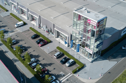 Luchtbeeld van een modern retailcomplex met meerdere winkels, ruime parkeergelegenheid en goede bereikbaarheid, ideaal voor een vlotte winkelervaring – X²O badkamers