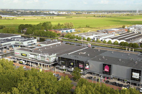 Luchtbeeld van een uitgebreid retailpark met diverse winkels, ruime parkeergelegenheid en een groene omgeving, vlot bereikbaar voor een aangename winkelervaring – X²O badkamers