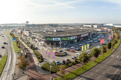 Overzicht van een grootschalig retailpark langs een drukke invalsweg, met talrijke winkels, ruime parkeervoorzieningen en uitstekende bereikbaarheid – X²O badkamers