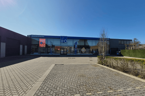 Façade d’un magasin XO Salles de Bains avec une large vitrine en verre, un grand parking vide et un ciel bleu par une journée ensoleillée.