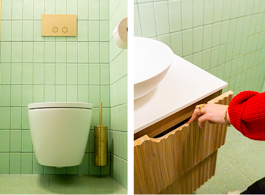 In deze x²o badkamers zie je links een waskom op een houten meubel met gouden kraan, in het midden een wandtoilet met gouden toiletborstel, en rechts een hand die een lade opent van het meubel.