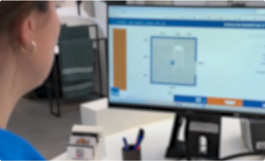 Une femme regarde un écran d’ordinateur affichant une application de planification de salle de bains. L’écran montre un plan 2D avec une douche et des dimensions. Cet outil numérique reflète les services de conseil proposés par x²o salles de bains.