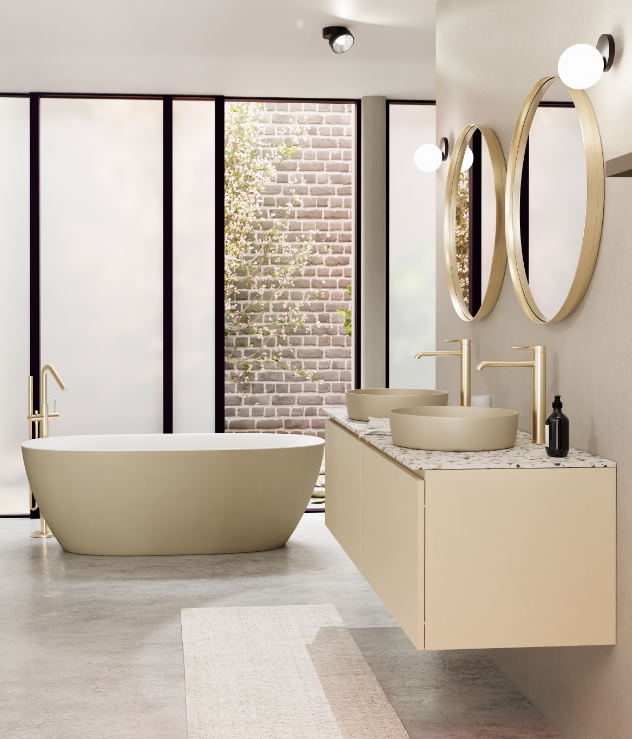 Salle de bain luxueuse avec une baignoire autoportante, un meuble suspendu beige avec un plan en terrazzo, deux vasques et des accents dorés, y compris des miroirs ronds et des robinets.