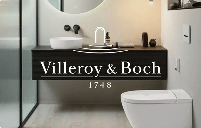 Salle de bains élégante chez X²O Salles de bains, équipée de sanitaires Villeroy & Boch. À gauche, un meuble-lavabo suspendu noir mat avec une vasque ronde blanche posée et un robinet mural noir. Un grand miroir rond rétroéclairé est accroché au-dessus. À droite, un WC moderne blanc et compact est installé. L’ambiance est minimaliste avec des tons neutres, une niche murale décorative et une paroi de douche en verre dépoli. Le logo Villeroy & Boch avec la mention “1748” est placé au centre de l’image.
