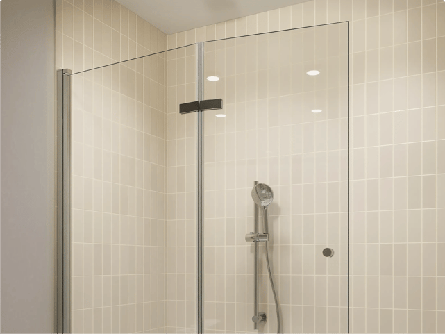 Paroi de douche en verre transparent avec profilé noir, installée devant des carreaux métro couleur crème posés verticalement et une douchette chromée, dans une salle de bains de x²o salles de bains.