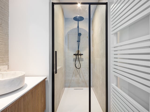 Lavabo en marbre, douche à pluie noire dans cabine en verre et radiateur.