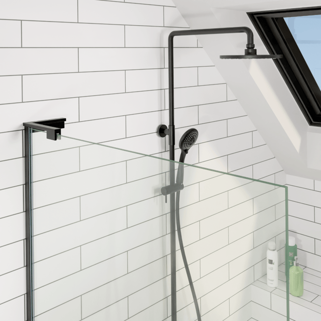 Douche moderne de X²O salles de bains dans une salle de bain mansardée avec fenêtre de toit, carrelage mural blanc rectangulaire, paroi de douche en verre transparent et colonne de douche noire avec douche pluie et douchette.
