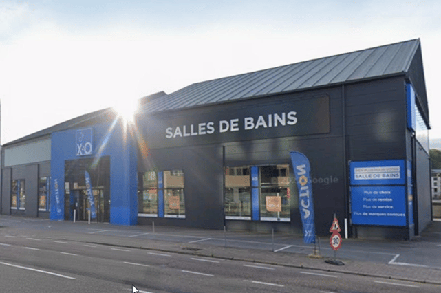 Magasin X²O salles de bains avec façade sombre, grandes vitrines et lumière du soleil à l’avant – X²O salles de bains