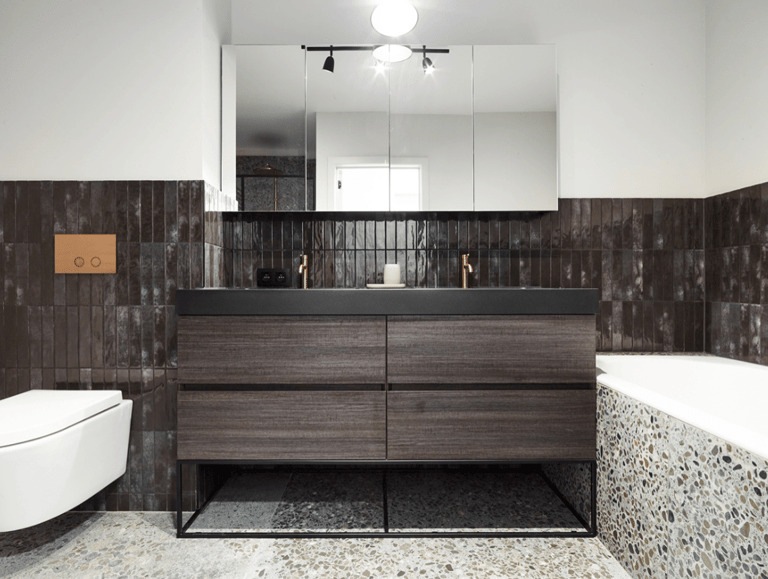 Salle de bains moderne et industrielle de x²o salles de bains avec un meuble double vasque en bois foncé, un plan de toilette noir avec deux vasques intégrées, des robinets en cuivre, des carreaux muraux foncés et une grande armoire miroir au-dessus.
