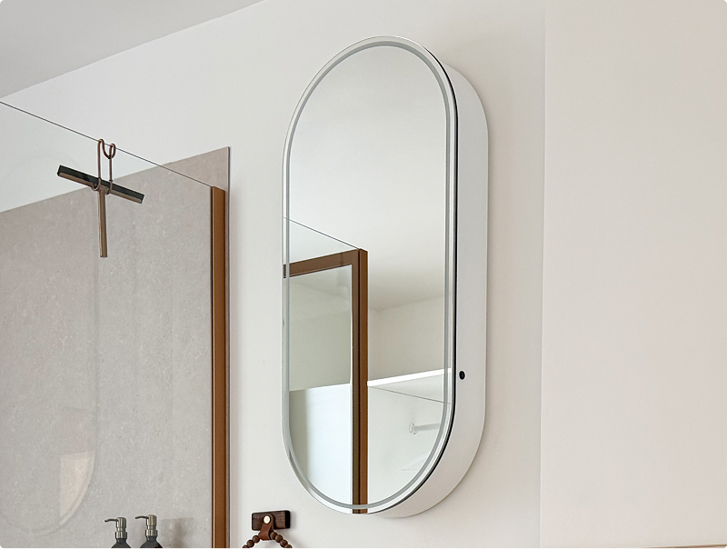 Ovale badkamerspiegel van x²o badkamers met anti-damp functie, geplaatst boven een wastafel naast een douchewand in een lichte ruimte.