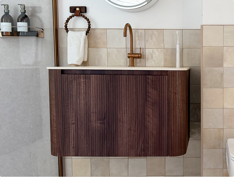 Close-up van een walnoot houten wastafelmeubel van x²o badkamers met afgeronde vormen en roségouden kraan.