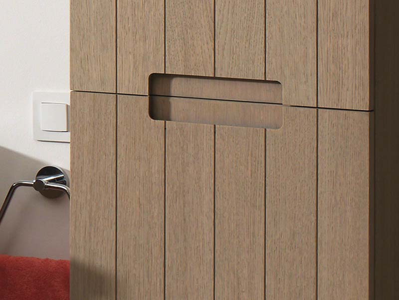 Detail van een houten badkamerkast met verticale lijnen en geïntegreerde handgreep voor een strak design.