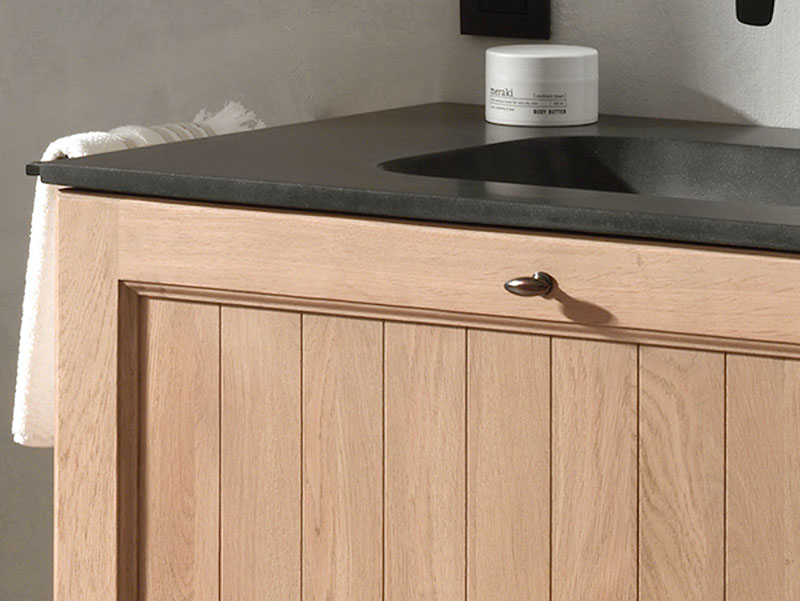 Detail van een houten wastafelmeubel met donker stenen blad, ingebouwde wastafel en klassieke ladeknop.