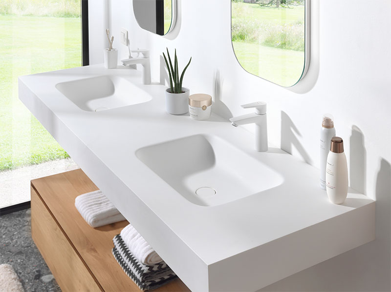 Minimalistische dubbele wastafel in wit solid surface met geïntegreerde wasbakken en moderne kranen.