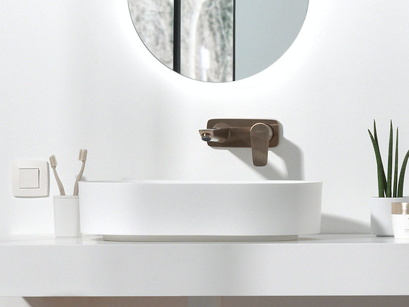 Witte opzetwaskom met wandkraan in brons en ronde spiegel met verlichting, modern en stijlvol design.