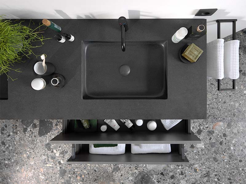 Meuble de salle de bain noir avec lavabo intégré, tiroir ouvert et produits de soin organisés.