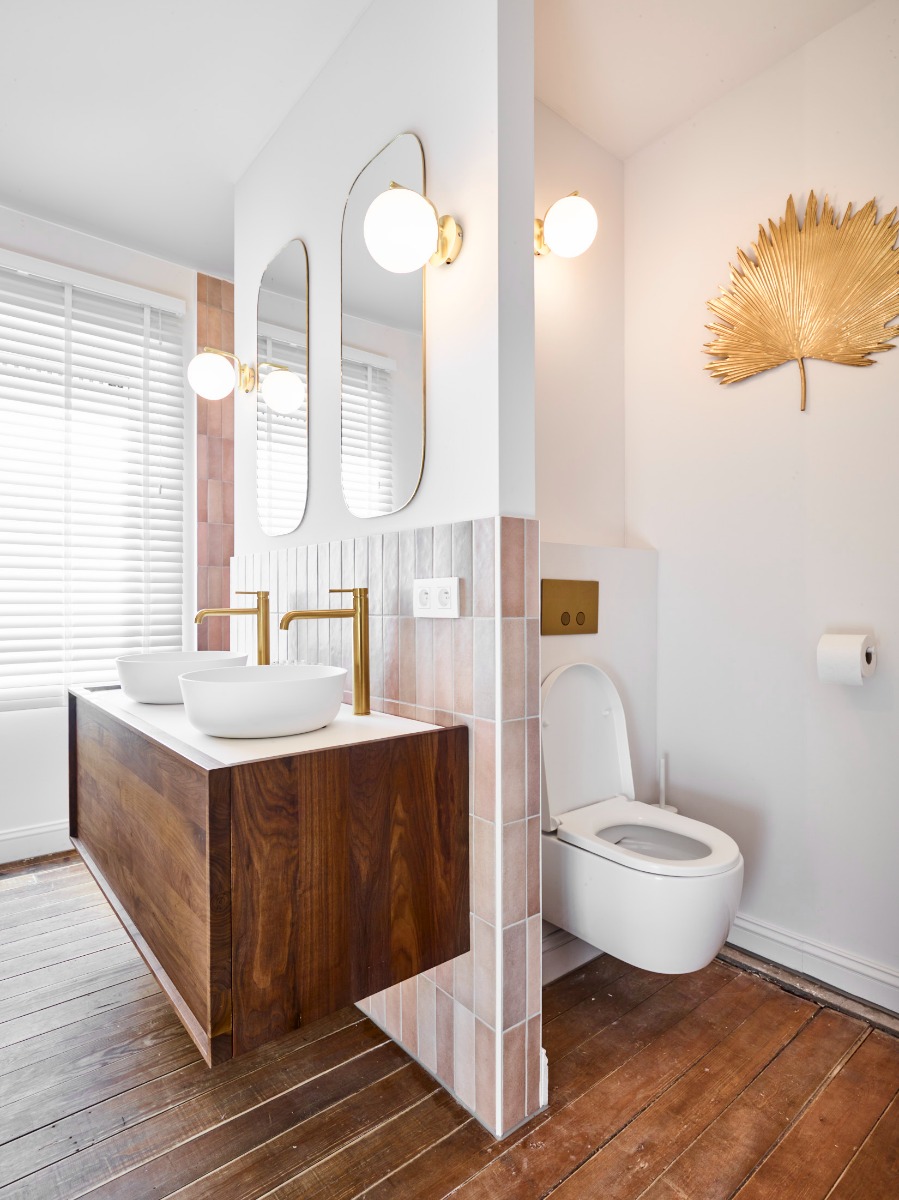 Moderne badkamer met een houten wastafelmeubel, gouden verlichting, twee ronde spiegels en een minimalistisch toilet