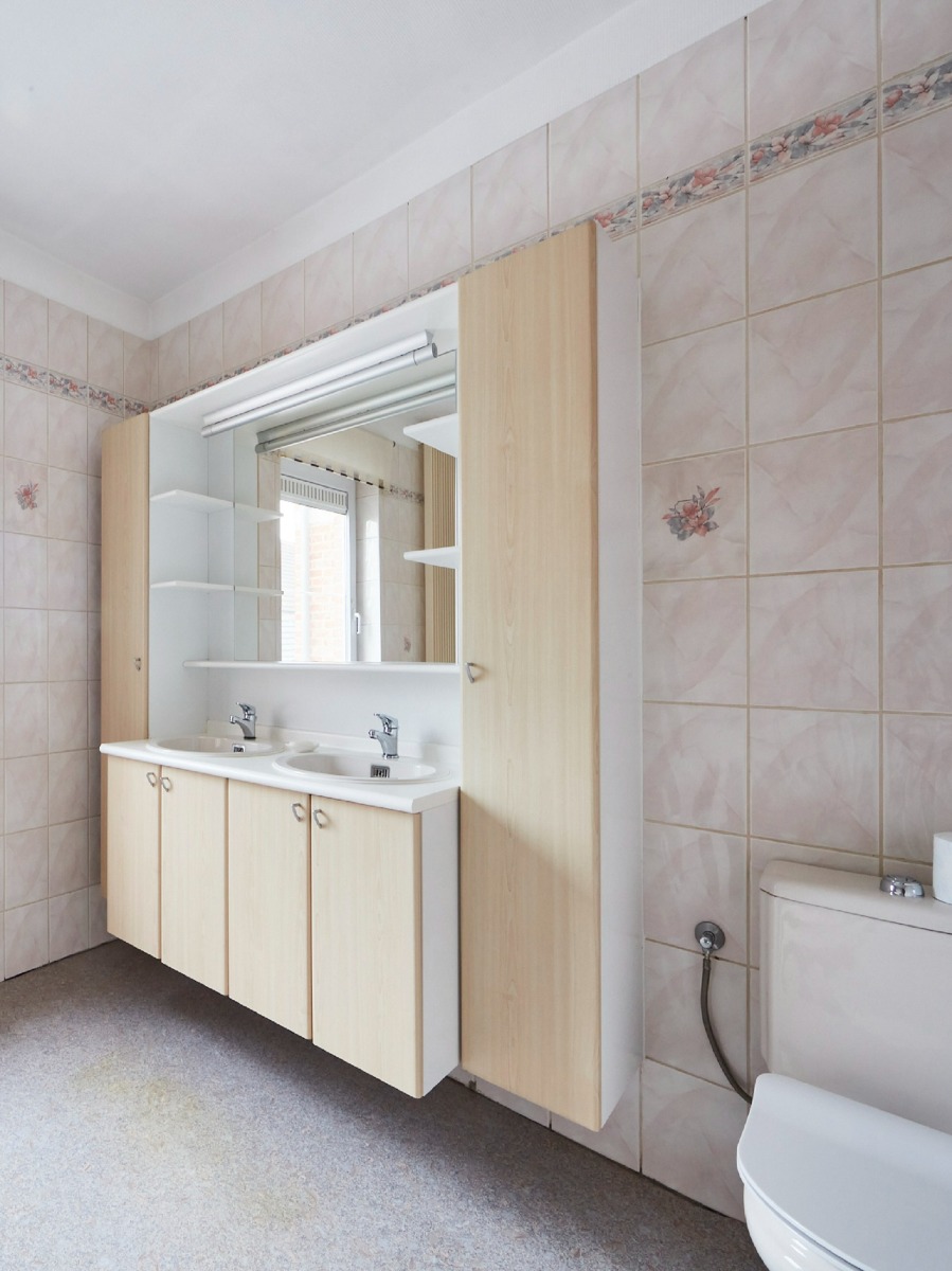 Badkamer met dubbele wastafel, toilet en opbergmeubel met beige tegels en vloerbedekking