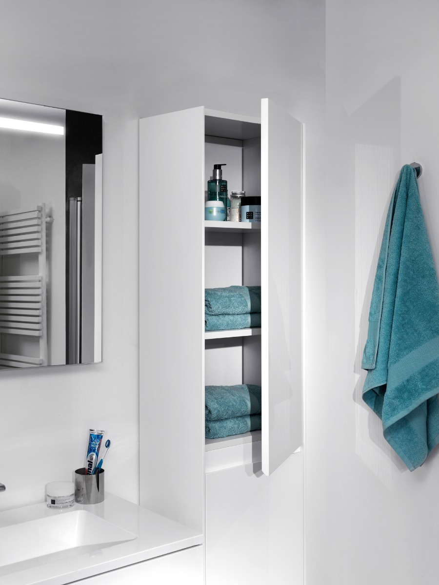Armoire de salle de bain blanche avec porte ouverte, contenant serviettes et produits de soins.