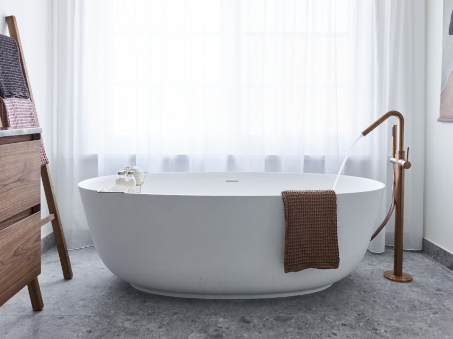 Salle de bains avec une baignoire îlot, un robinet doré et un sol en marbre gris.