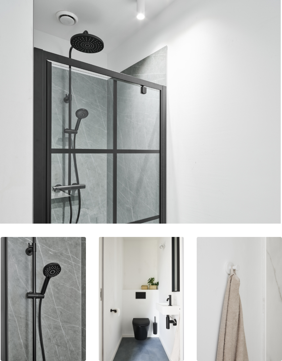 Vue d’ensemble d’une salle de bains industrielle robuste de x²o salles de bains avec un meuble de salle de bains noir à double vasque, des robinets noirs mats, un grand miroir éclairé, des murs blancs et un sol carrelé gris au style moderne.