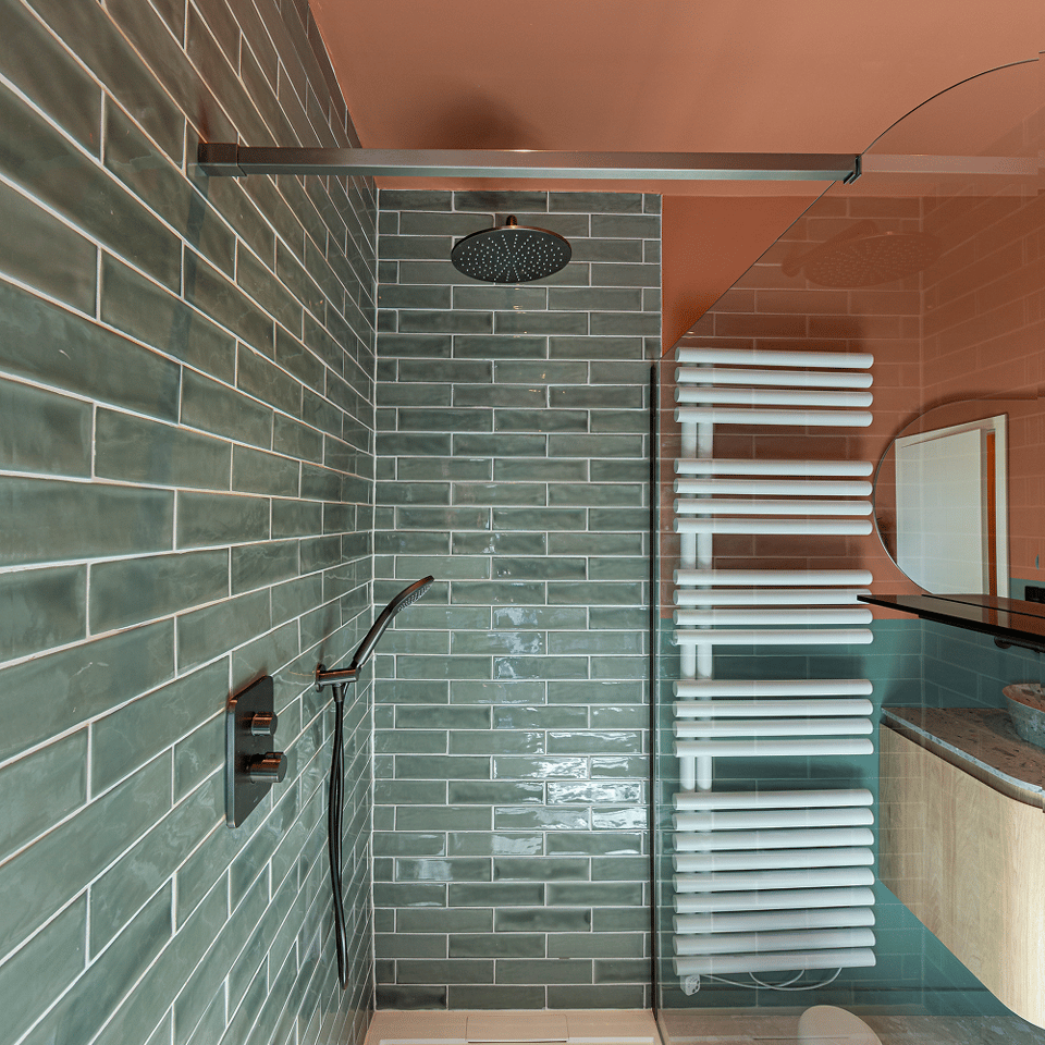 Inloopdouche met groene glanzende tegels, zwarte regendouche, handdouche, glazen wand en witte handdoekradiator.