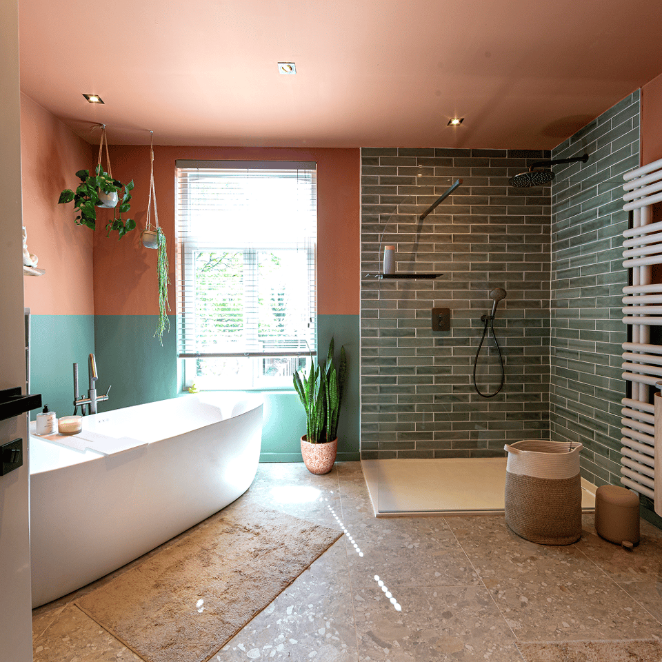 Moderne badkamer met vrijstaand bad, groene tegelwand, inloopdouche, terracotta en groene muren, houten jaloezieën en kamerplanten.