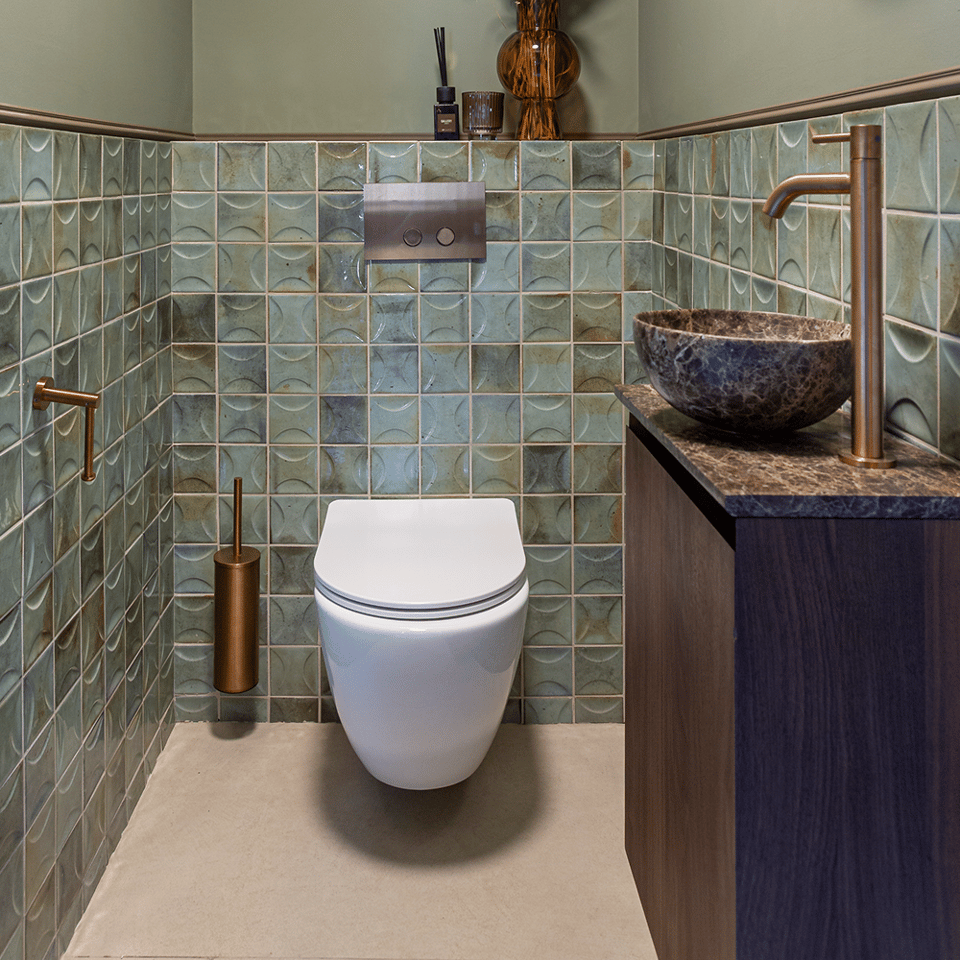 Toiletruimte met groene glastegels, hangtoilet, donker houten wastafelmeubel, natuurstenen waskom en koperkleurige accenten.