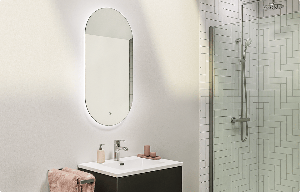 Ovale Storke Somma badkamerspiegel met geïntegreerde LED-verlichting rondom en anti-dampfunctie, gemonteerd boven een wastafel met chromen kraan naast een inloopdouche met glazen douchewand en witte wandtegels in een badkamer van x²o badkamers.