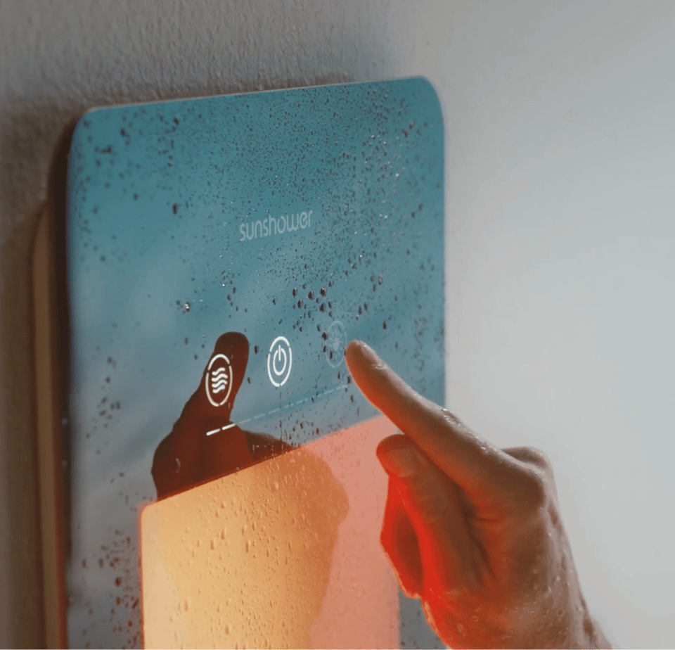 Main qui appuie sur le bouton tactile d’un panneau Sunshower avec surface en verre mouillée et lumière orange intense.