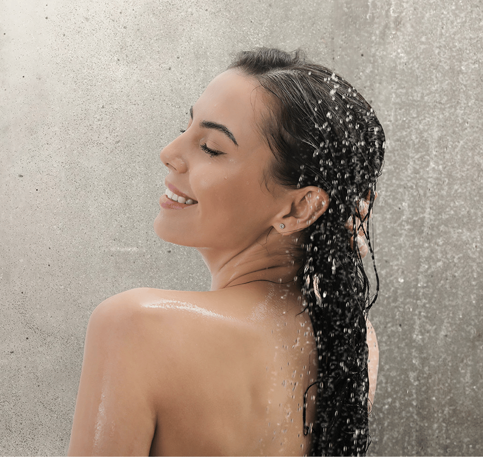 Femme profitant d'une douche relaxante dans une salle de bains de x²o salles de bains avec panneaux muraux Dumawall aspect béton, étanches et faciles à nettoyer.