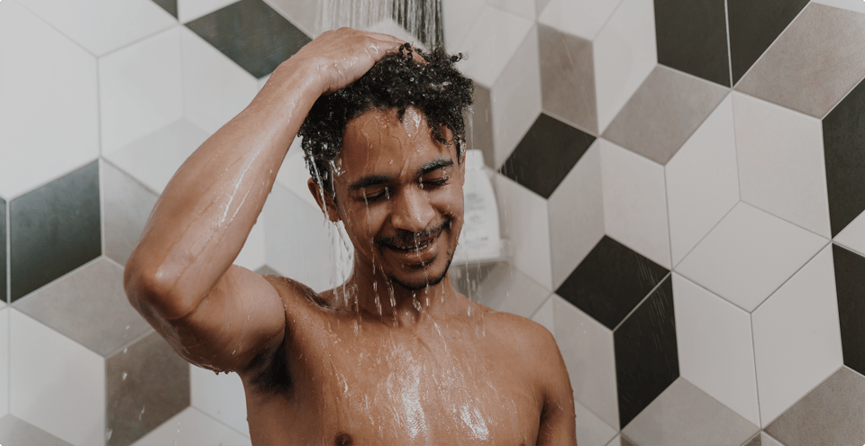 Mann genießt eine erfrischende Dusche in einem modernen Badezimmer mit geometrischen Fliesen – X²O Badezimmer