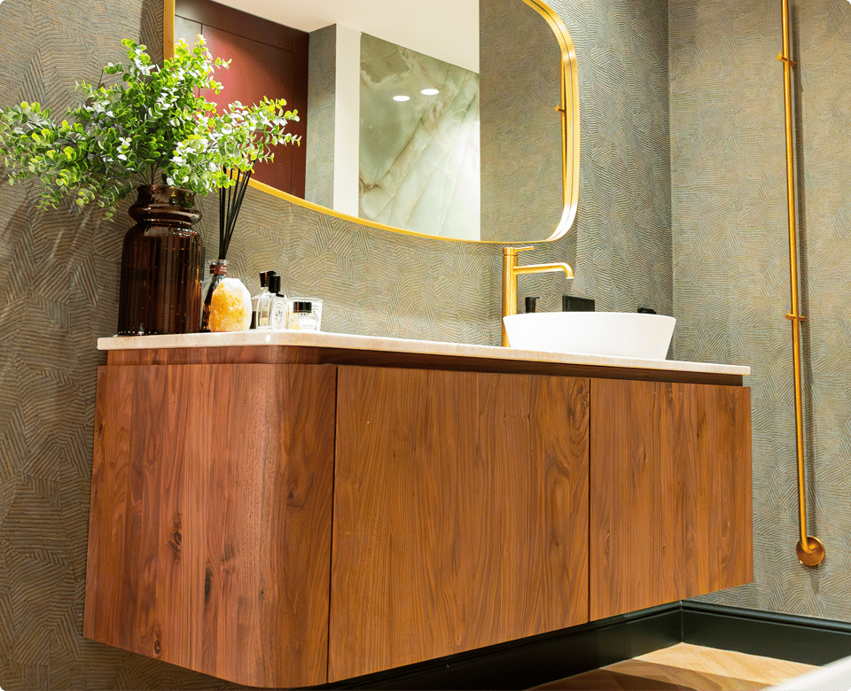 Deze foto laat een prachtig x²o badkamers detail zien: een groot ovaal vrijstaand bad met een gouden kraan en een handdoek. Ernaast staan grote groene planten en de vloer heeft een warme houtlook die de luxe uitstraling versterkt.