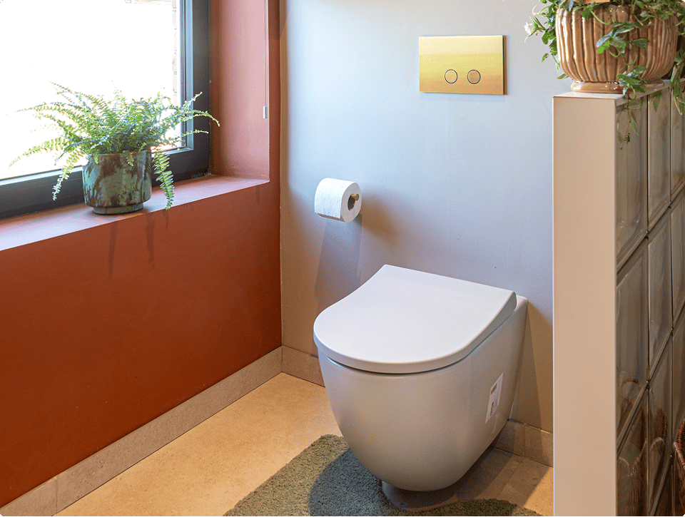 Modern Luca Varess Vinto hangtoilet van x²o badkamers naast een raam met planten, warme terracottamuur en minimalistische inrichting.