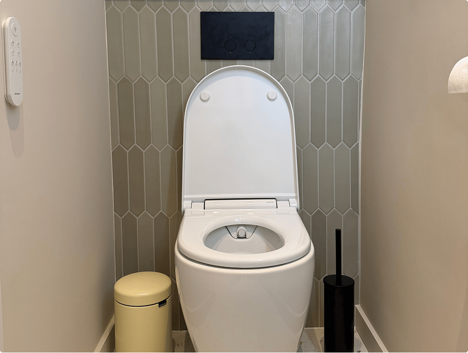 Weißes Geberit AquaClean Alba Dusch-WC von x²o Badezimmer in einem schmalen modernen Toilettenraum mit beigen Fliesen und schwarzen Accessoires.