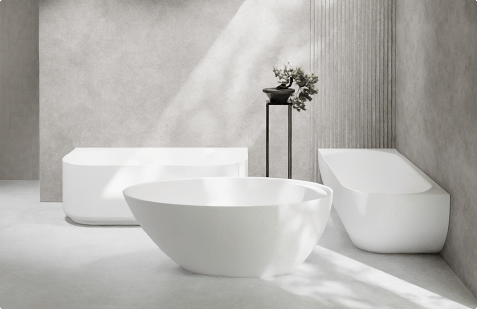Op deze foto zie je drie verschillende vrijstaande baden in een minimalistische x²o badkamers setting. Vooraan staat een rond wit bad met zachte lijnen, links een rechthoekig bad met strakke hoeken en rechts een ovaal bad met een schuine rugleuning. De baden staan op een lichte betonnen vloer tegen grijze wanden met een subtiel verticaal reliëf. Een zwarte hoge plantenstandaard met een klein boompje maakt het serene design compleet.