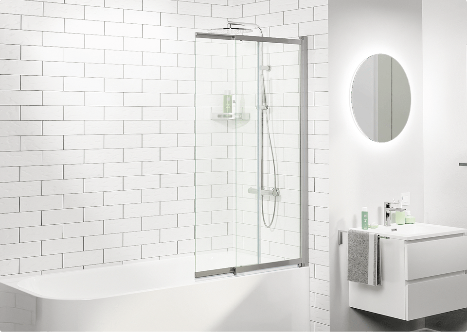 Salle de bains blanche moderne avec baignoire et paroi de bain en verre, carreaux métro blancs au mur, douche pluie avec douchette et meuble lavabo suspendu avec miroir rond, aménagée avec des produits de x²o salles de bains.