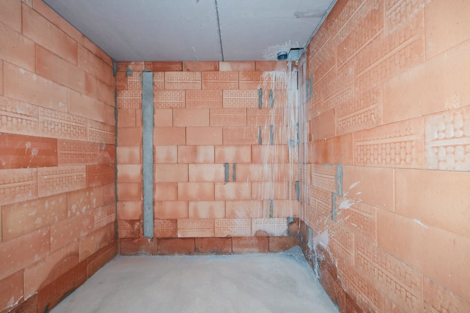 Ruwbouw van een badkamer met rode bakstenen muren en leidingen.