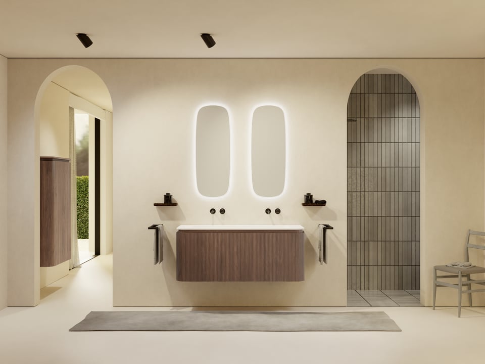 Moderne badkamer met een zwevend houten badkamermeubel met verticale ribstructuur, een lange witte wastafel met twee kranen en twee langwerpige spiegels met zachte led-achterverlichting. Links en rechts zitten nisplankjes met accessoires, er hangt een handdoek aan de zijkant en rechts is een boogopening naar een douchehoek met verticale wandtegels.