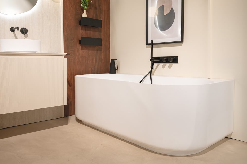 Photo de détail d’une salle de bains x²o salles de bains montrant une douchette noire et une paroi de douche en verre avec profils noirs sur un mur clair texturé.