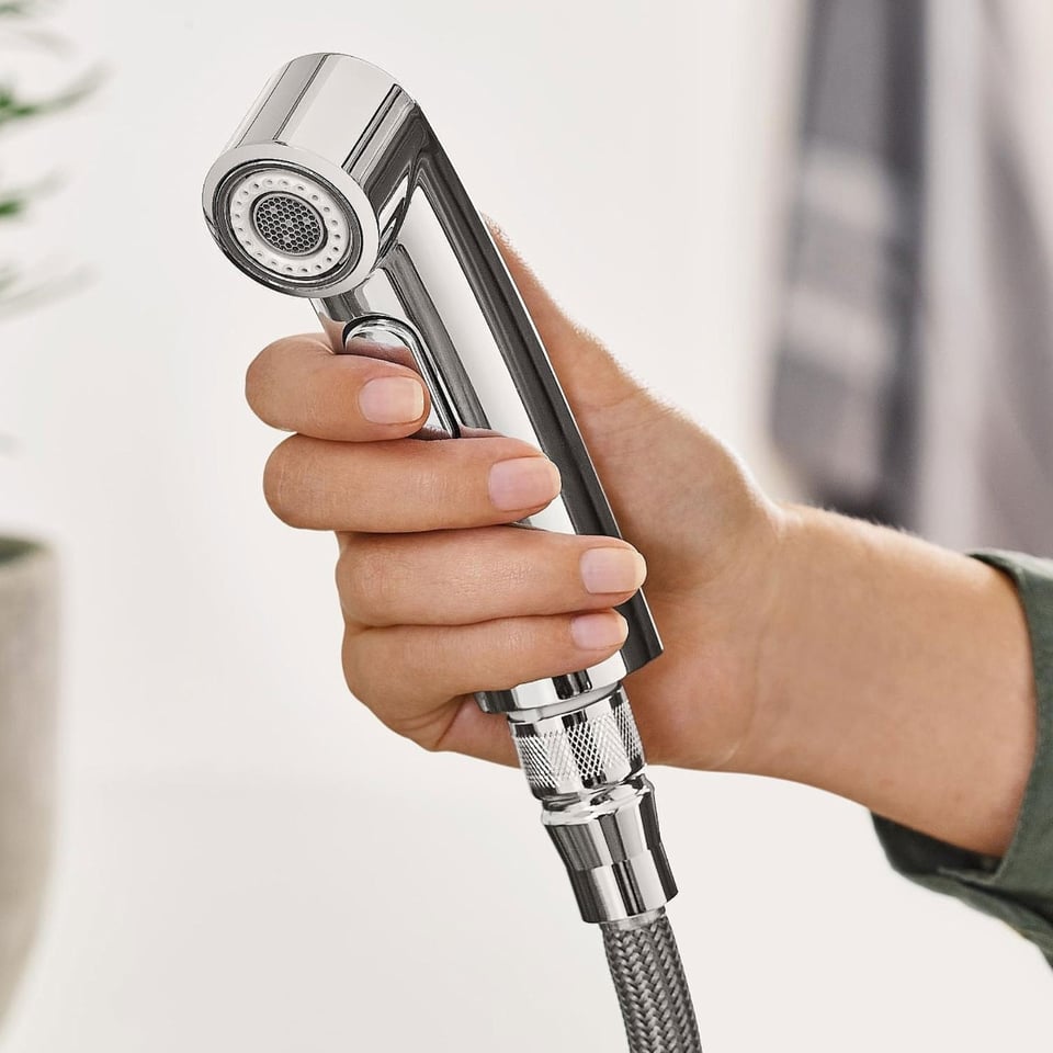 Chromen handdouche met een slangenbuis, vastgehouden door een hand.