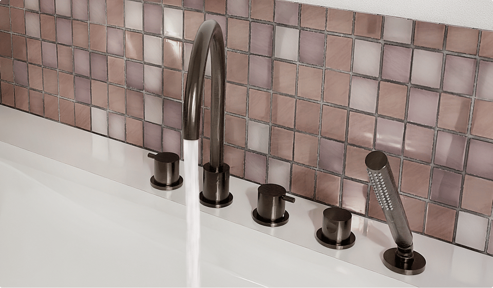 Detail van een badrand met elegante bronzen mengkranen, handdouche en sierlijke mozaïektegels in zachte roze en paarse tinten. Een luxueuze afwerking met metallic accenten in x²o badkamers.