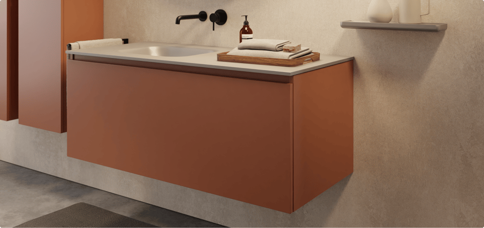  Warme x²o badkamers sfeer met een zwevend roestkleurig badkamermeubel, matzwarte kraan en ronde spiegel met zwarte rand. De beige wand en accessoires zoals het houten dienblad en keramiek op het wandplankje brengen een aardse, rustgevende uitstraling.